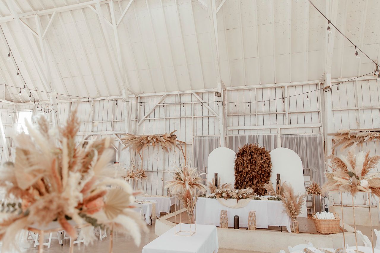 Wedding reception tent with boho decor featuring pampas grass arrangements and soft string lights overhead.