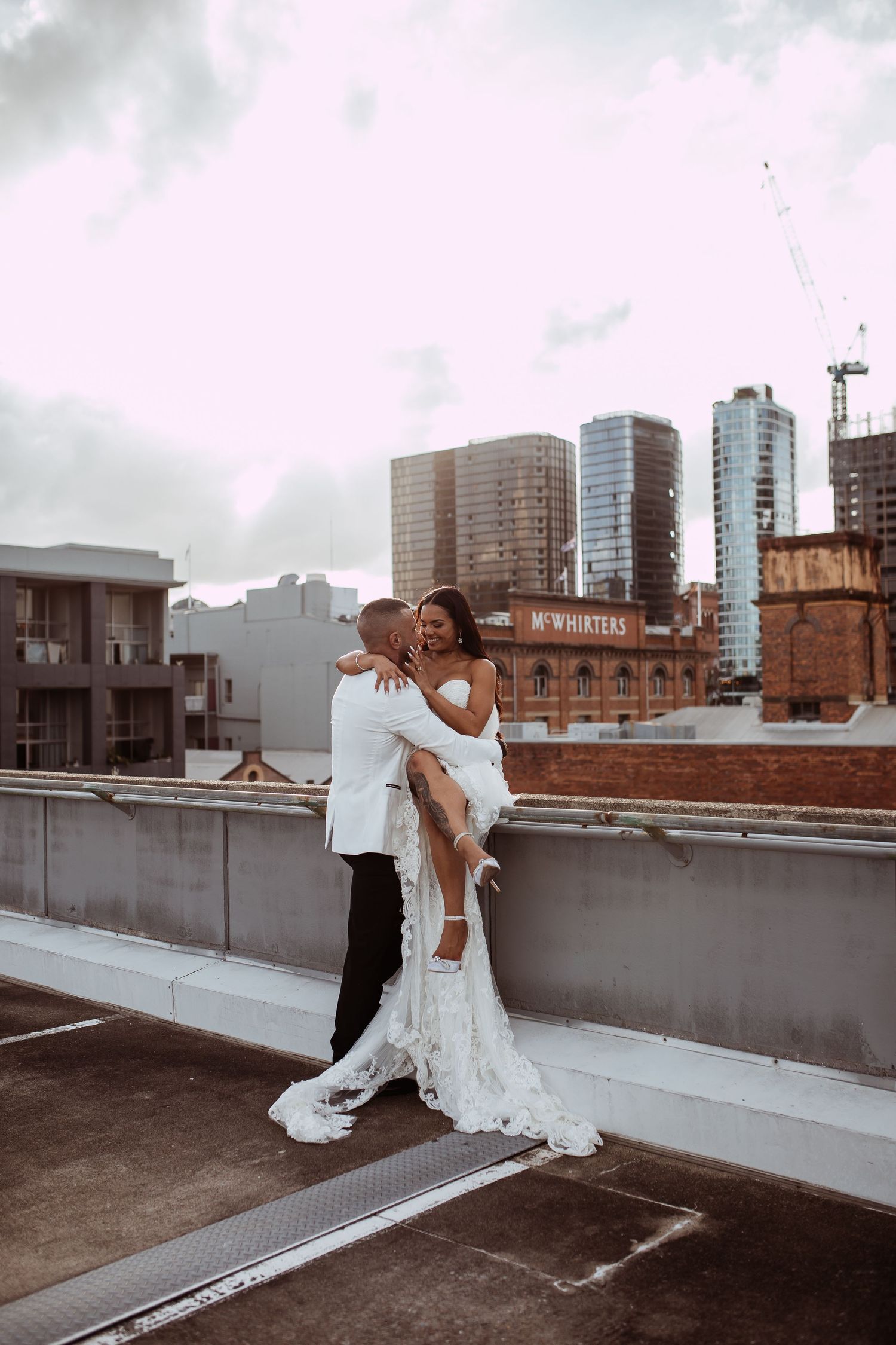 Urban rooftop parking garage wedding photo with couple embracing against city skyline and tall buildings in background.