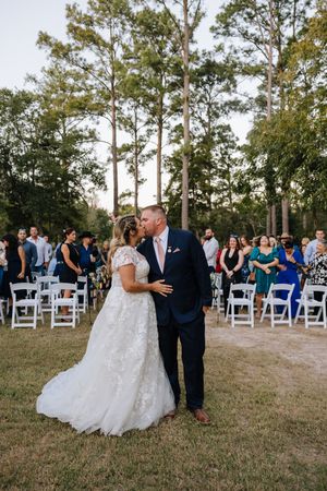A bride and groom share their first kiss as a married couple while guests celebrate in an outdoor ceremony.