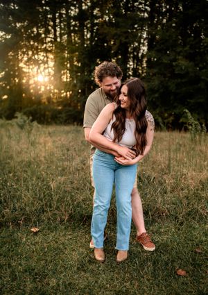 Romantic couple embrace in sunlit field during golden hour.
