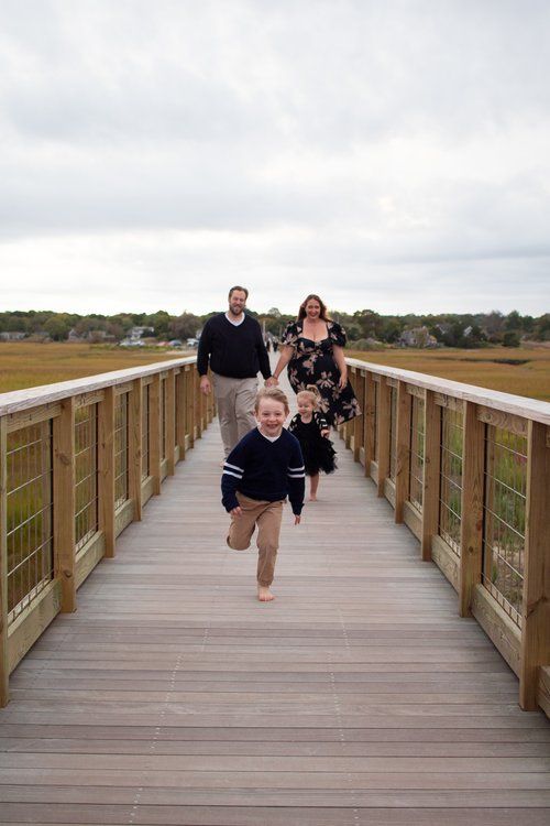A child runs joyfully on a wooden boardwalk while adults follow behind.