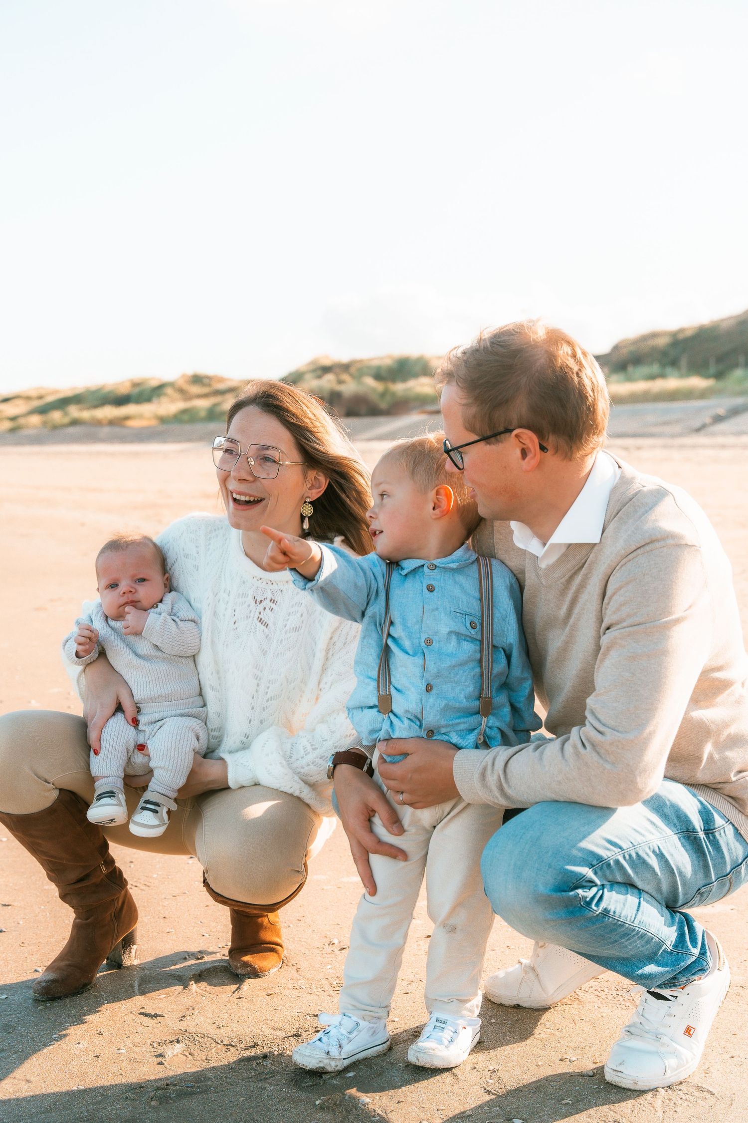 Happy family of four sitting together on sandy beach during golden hour.