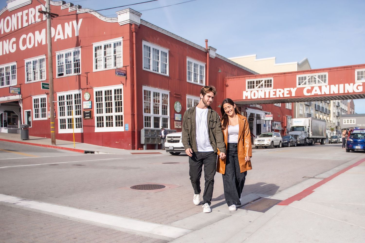 Couple strolling past the red Monterey Canning Company building on a sunny day.