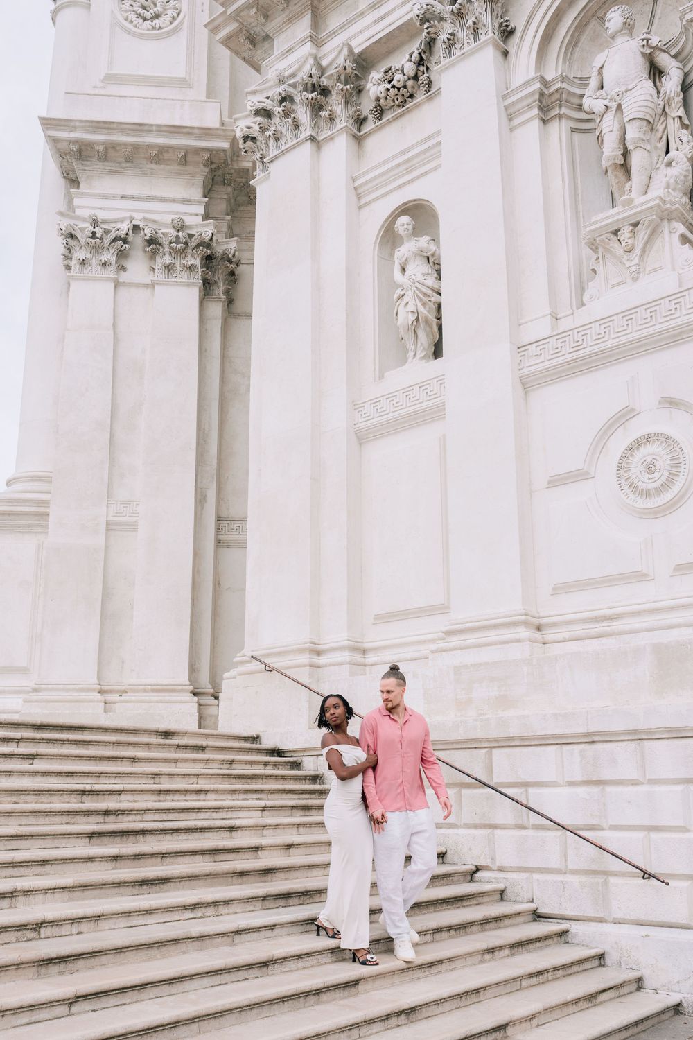 Interracial couple walking down marble steps of a grand white classical building in Venice, Italy.