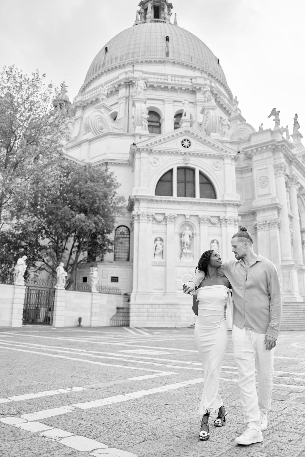 Black and white photo of couple posing in front of Santa Maria della Salute basilica in Venice, Italy.