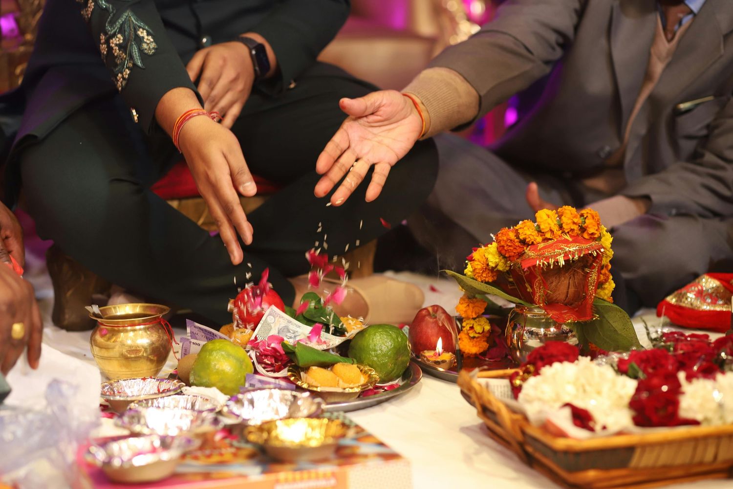 Hands performing Hindu puja ritual with traditional offerings, flowers, and sacred items on a decorated ceremonial plate.