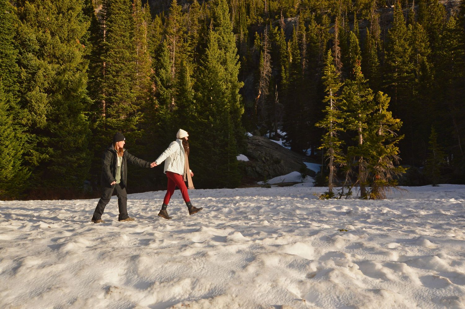 Female couple holding hands as they walk through a clearing at Dream Lake after their proposal. The Rocky Mountain Proposal Photographer