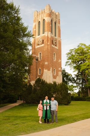 Graduate in green stole poses with family in front of Beaumont Tower at Michigan State University.