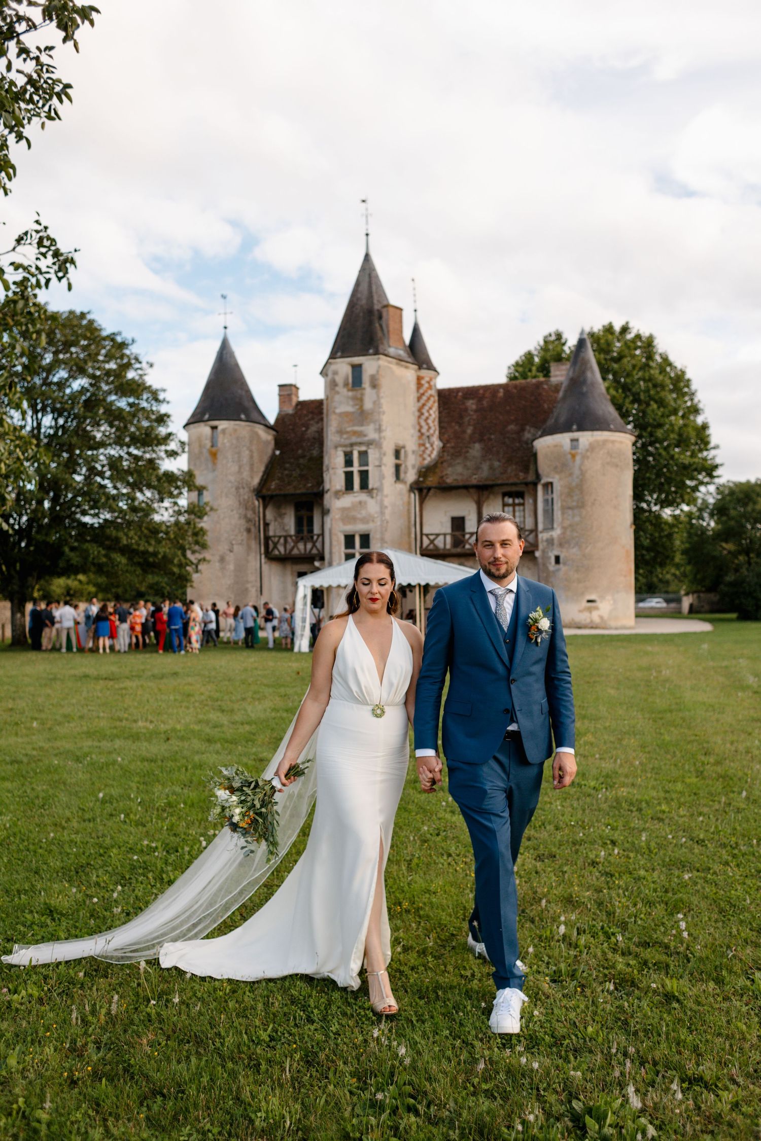 Bride and groom walk hand in hand with stunning French chateau in background.