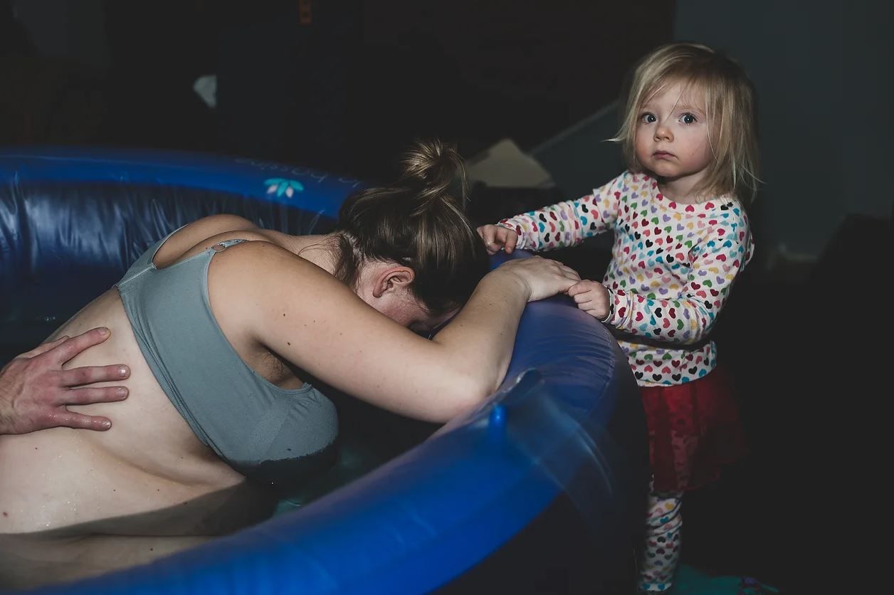 Birth scene in a dimly lit room with a blue inflatable pool.