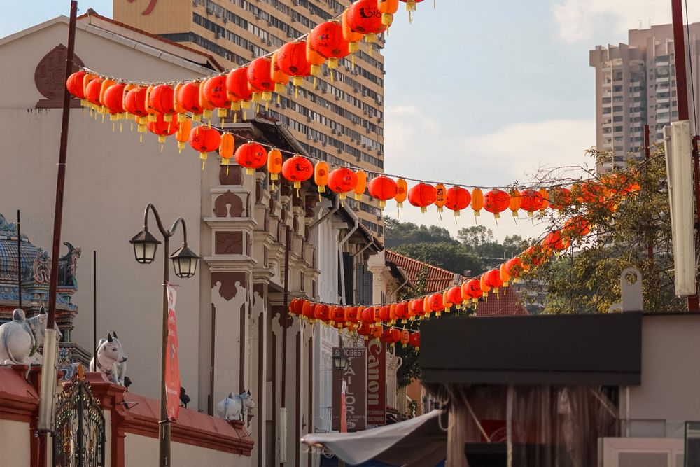 Red Chinese lanterns strung between colorful shophouses in Singapore's vibrant Chinatown district with city skyline.