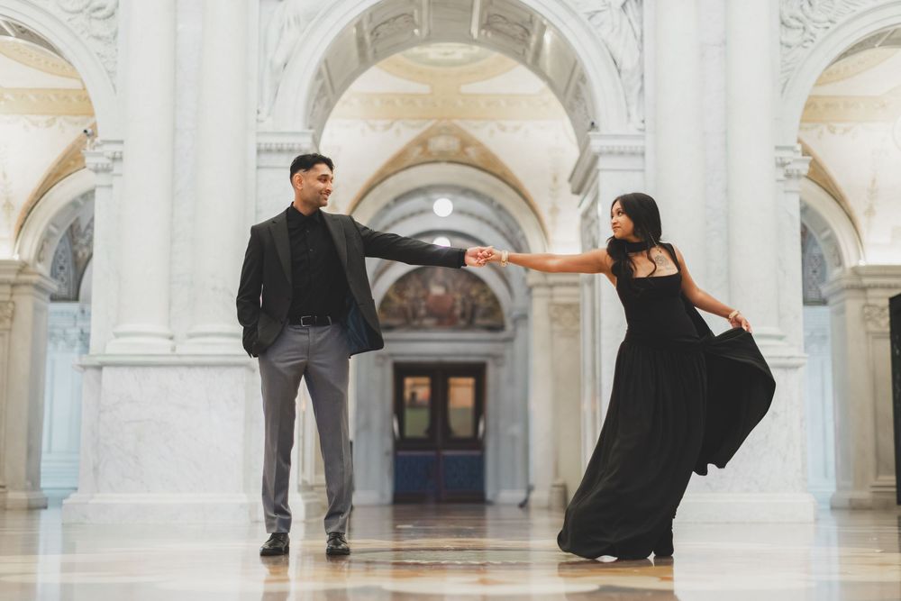 Elegant couple in black formal wear dancing in a grand marble hall with arched ceilings during their library of congress engagement