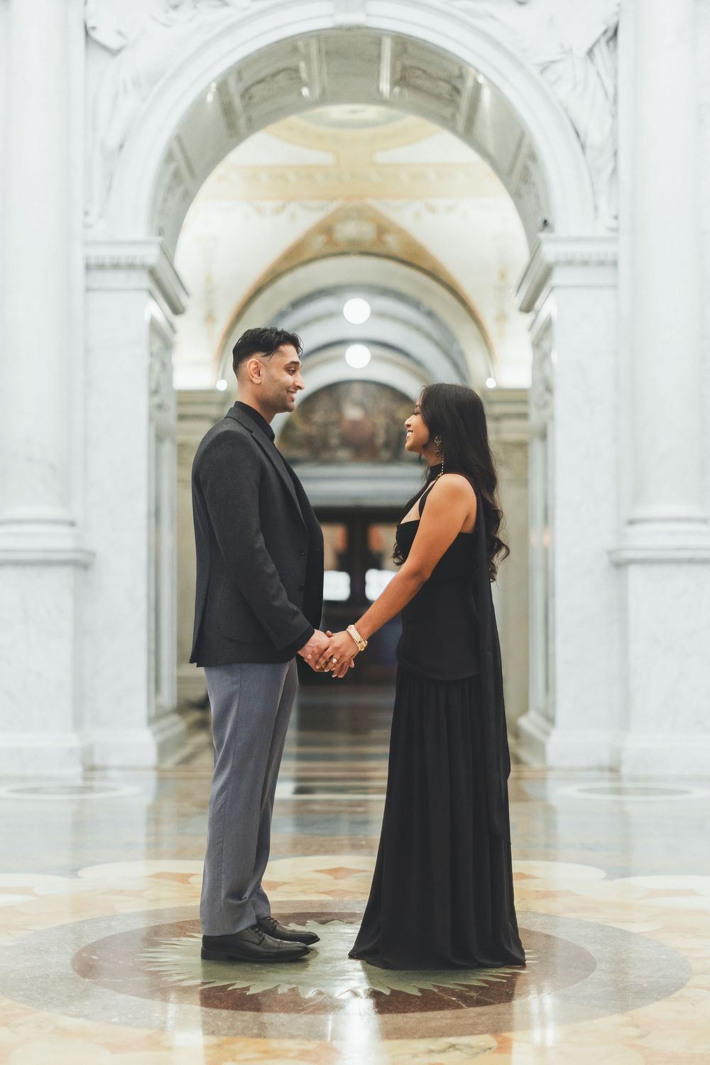 Couple in black formal attire holding hands in an elegant white marble hall with arched columns, library of congress photography