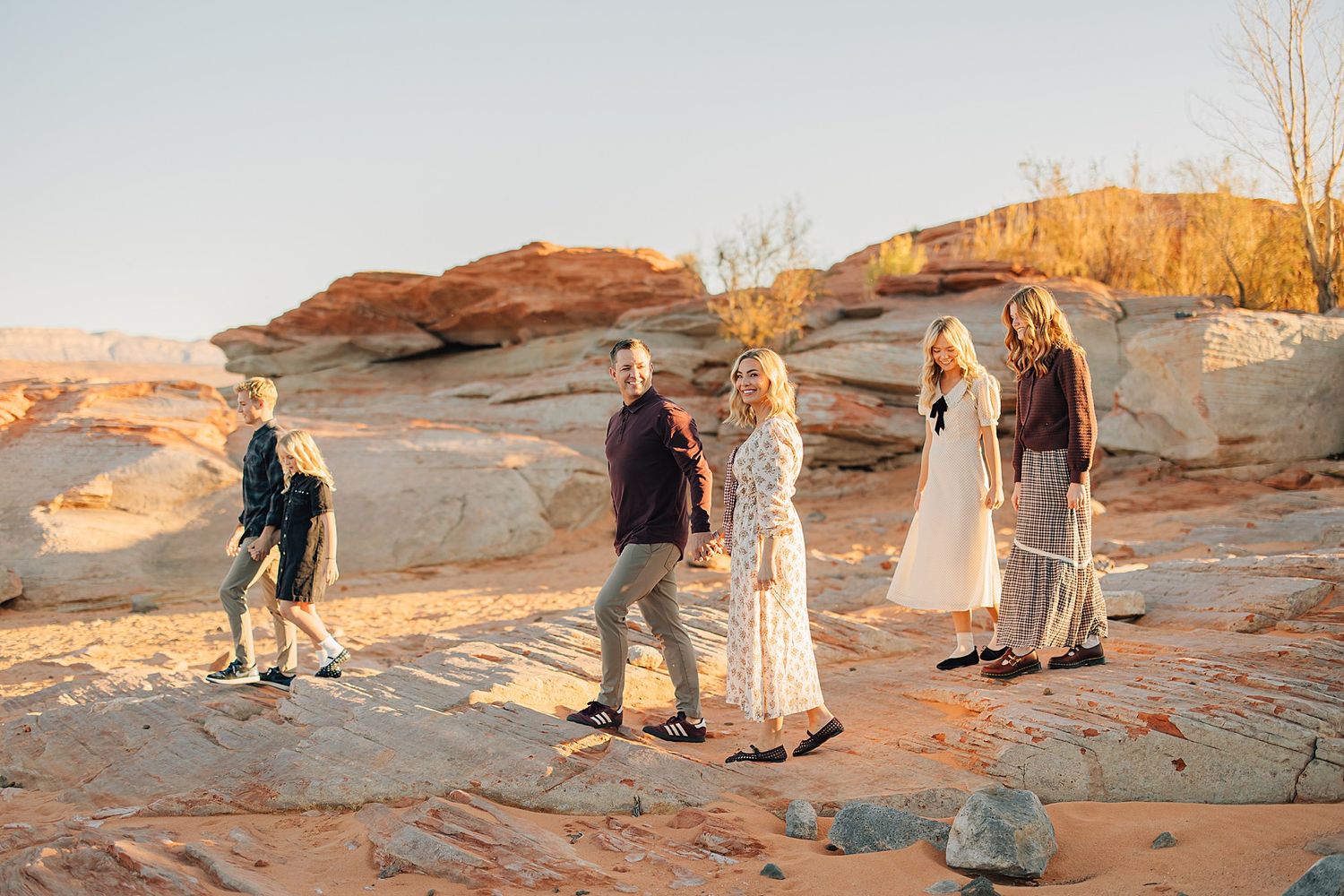 Family gathering on red rock desert landscape at golden hour in a scenic canyon setting.