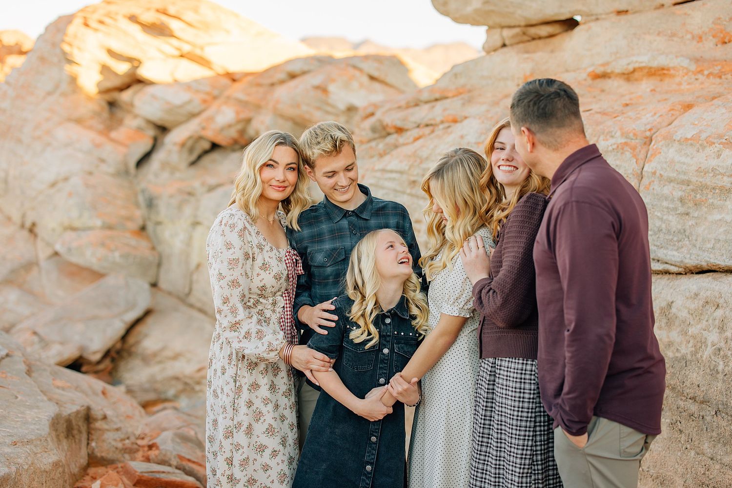 Family of five smiling together outdoors among rocky desert formations in warm golden light.