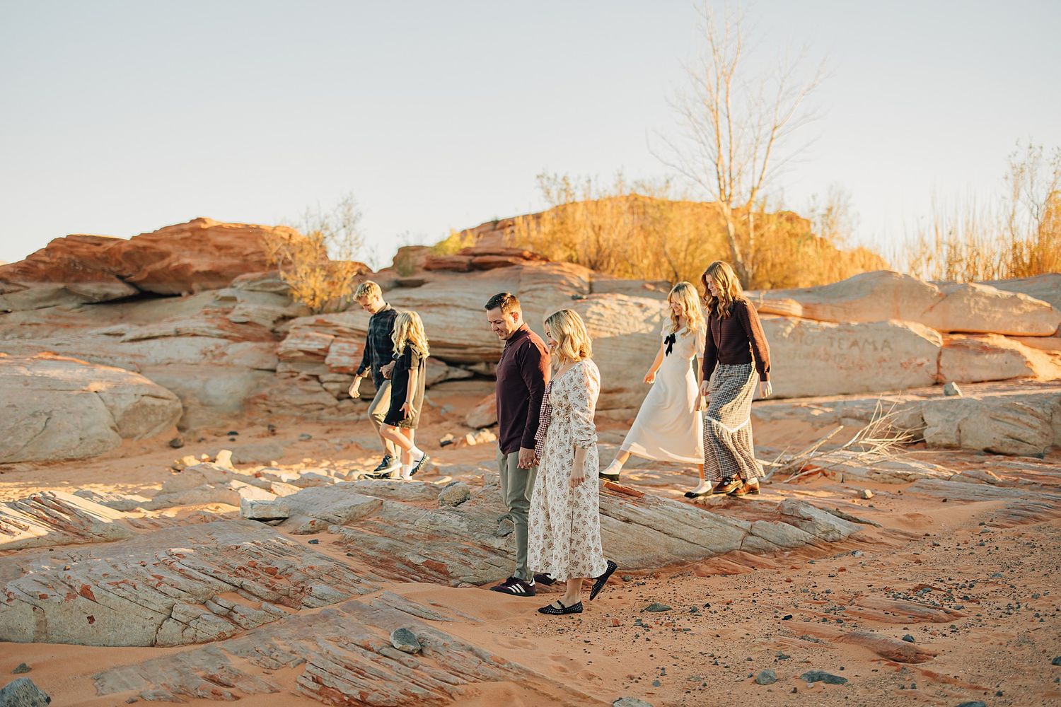 Four people walking on red sandstone rock formations in a desert landscape during golden hour sunset.