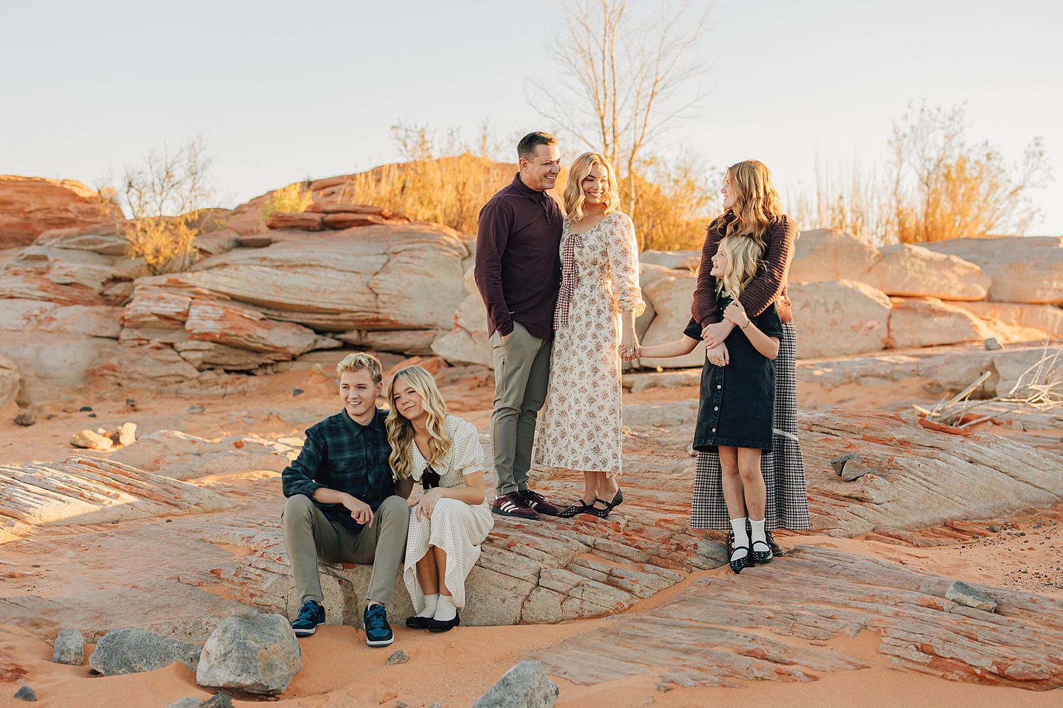 Family of five posing on red sandstone rocks in a desert landscape at golden hour sunset.
