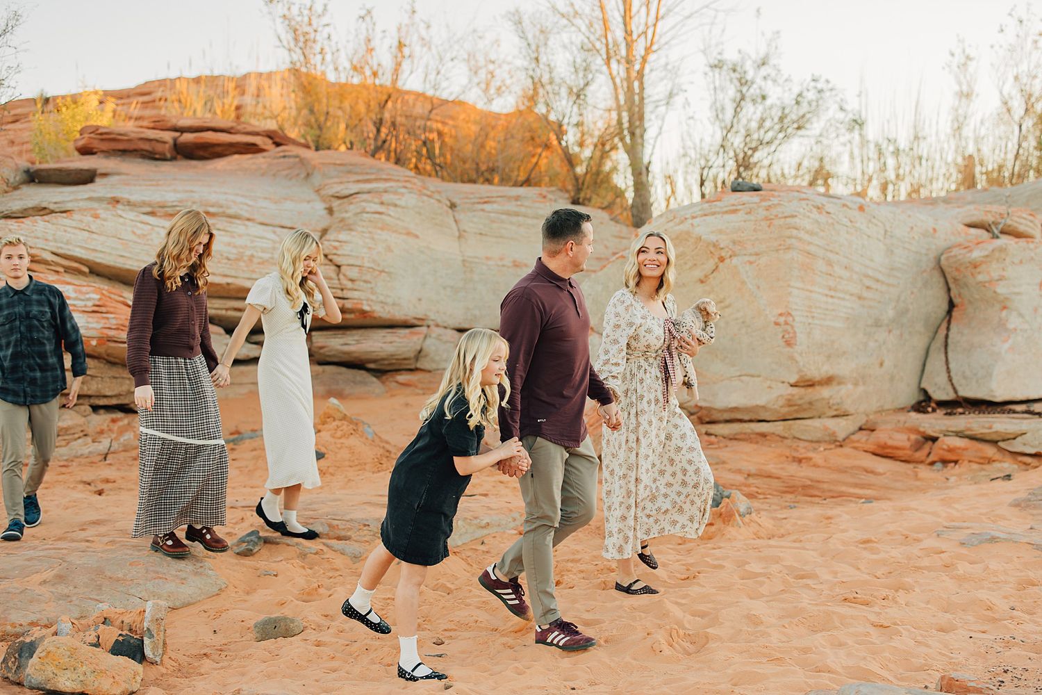 Family playing and dancing together on red rock desert landscape during golden hour outdoor photo session.