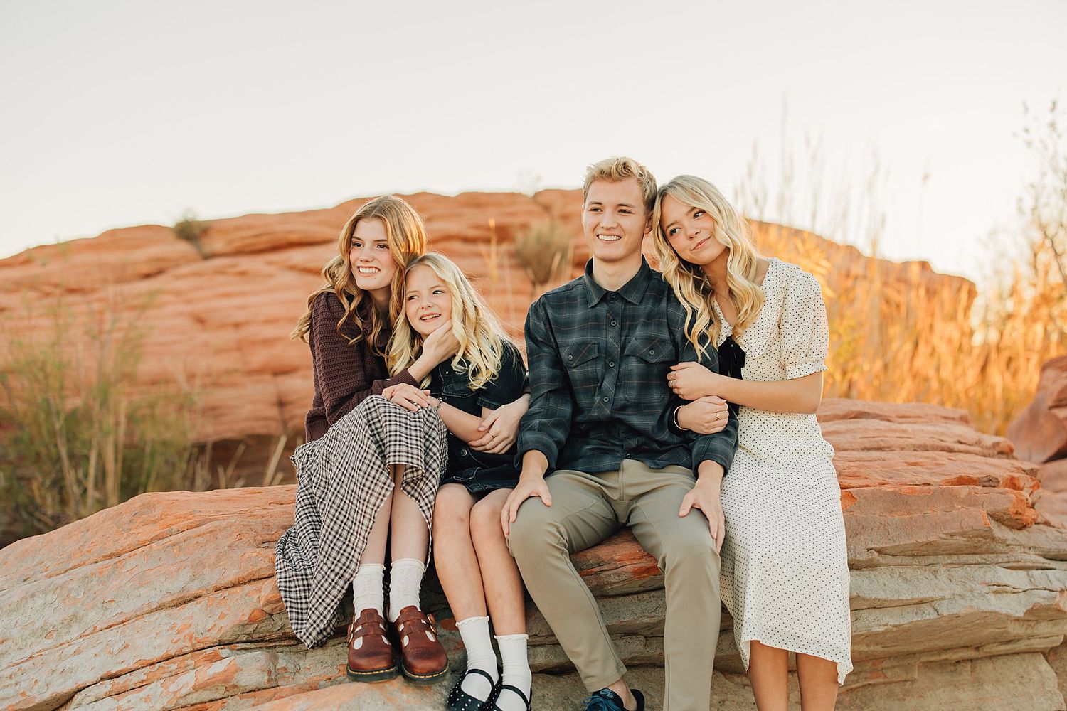 Family of four smiling together on red rock formations at golden hour in a scenic outdoor setting.