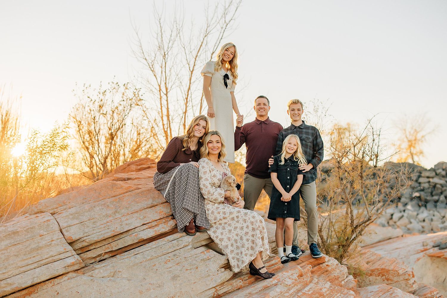 Family of five posing on sandstone rocks during golden hour sunset in a desert landscape.