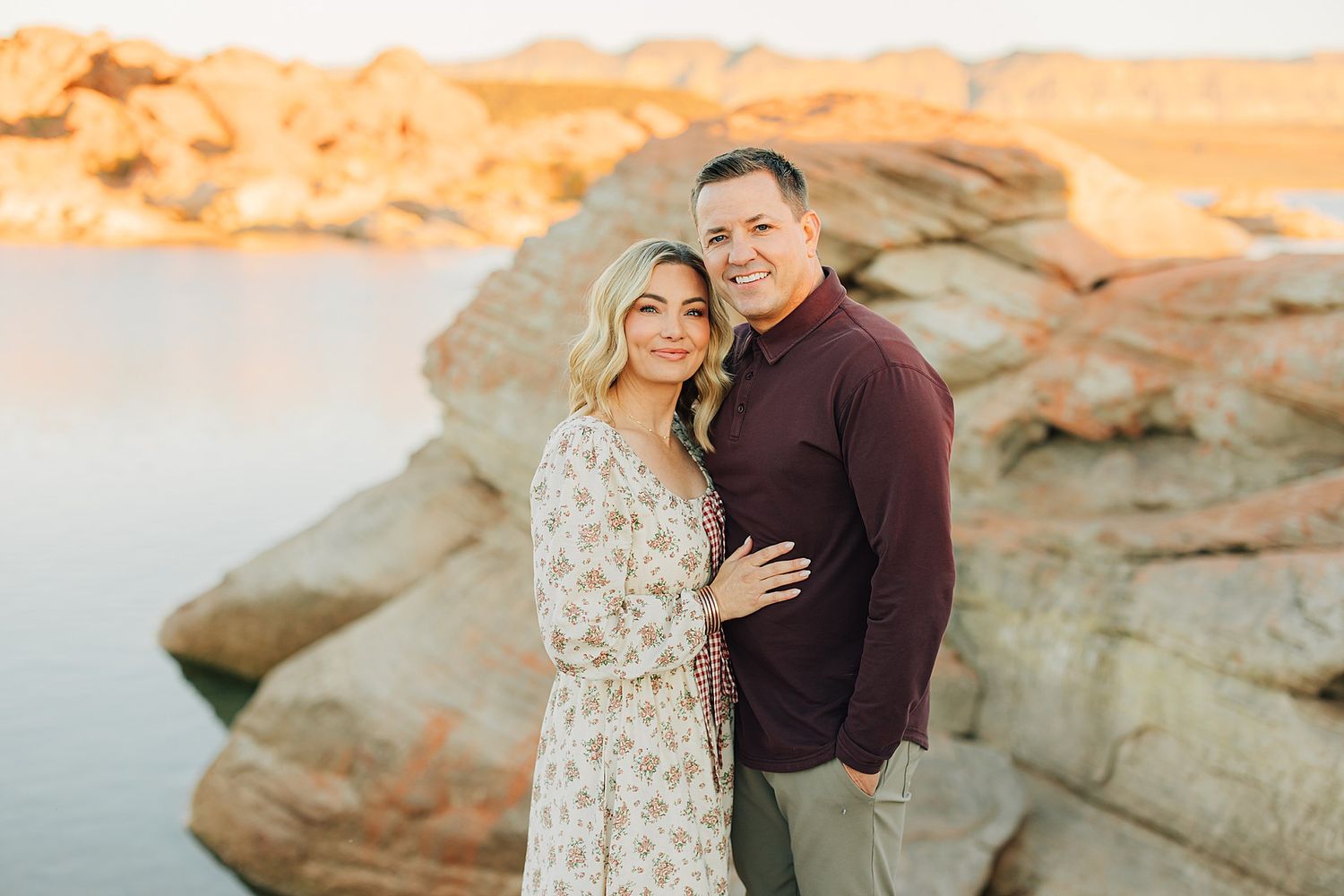 Smiling couple embracing in front of rocky desert landscape with glowing golden hour lighting.