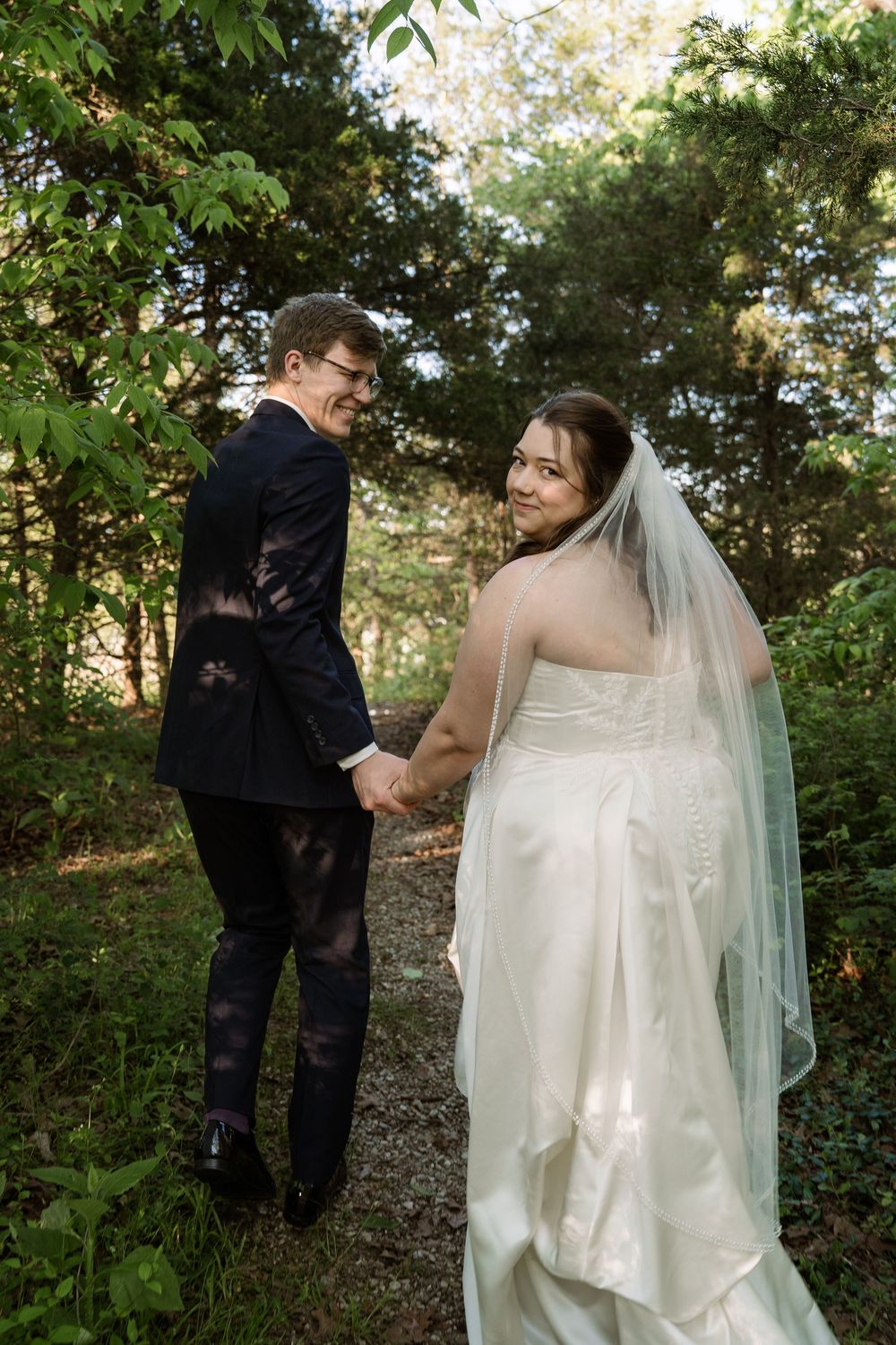 ©AnnaVonRiesenPhotography Bridal Portraits | Color image of a couple walking into a green forest.