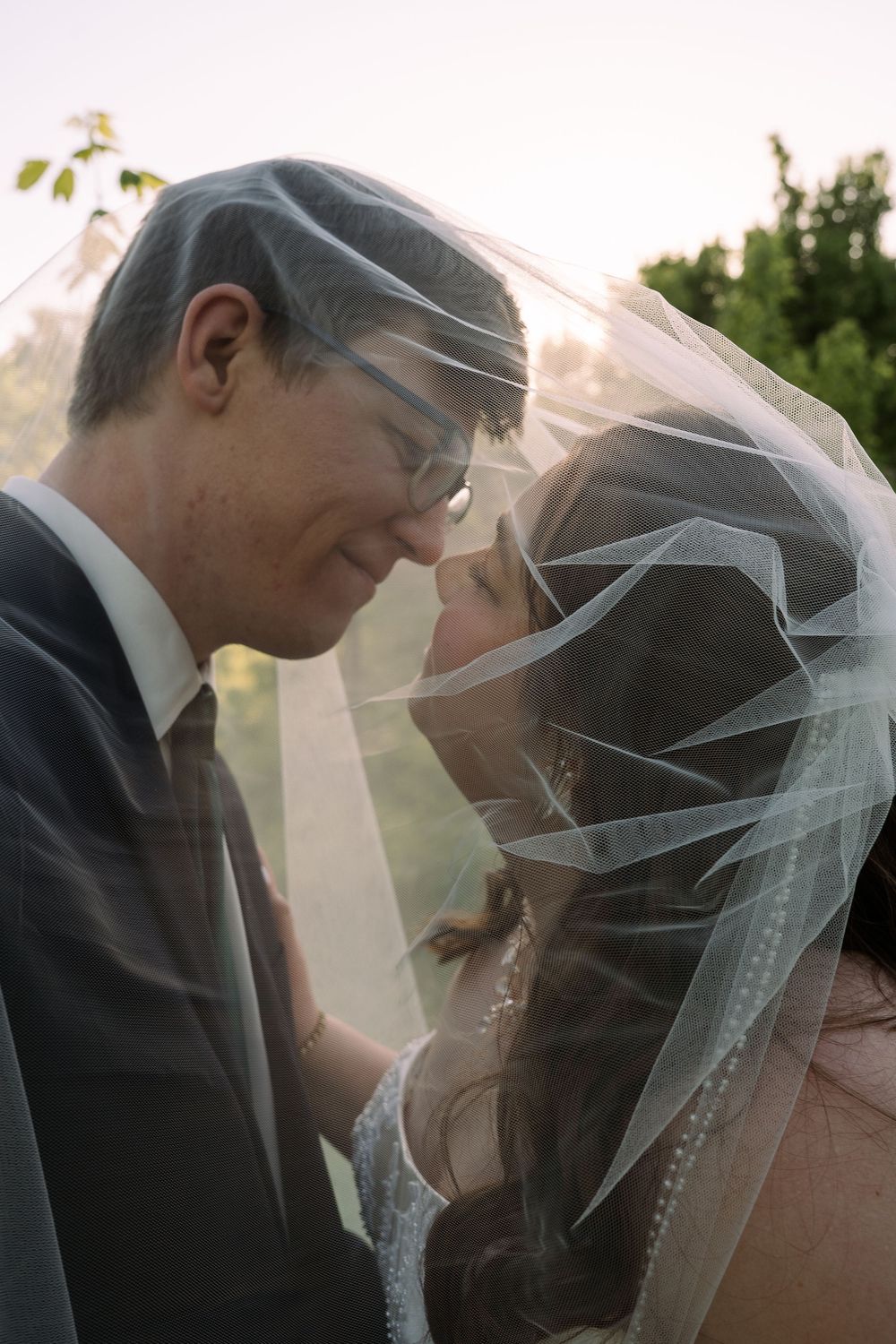 ©AnnaVonRiesenPhotography Bridal Portraits | Color image of a couple leaning in for a kiss under a veil.