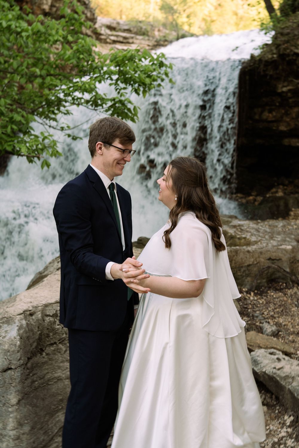 ©AnnaVonRiesenPhotography Bridal Portraits | Color image of a couple smiling at each other with a waterfall in the background.