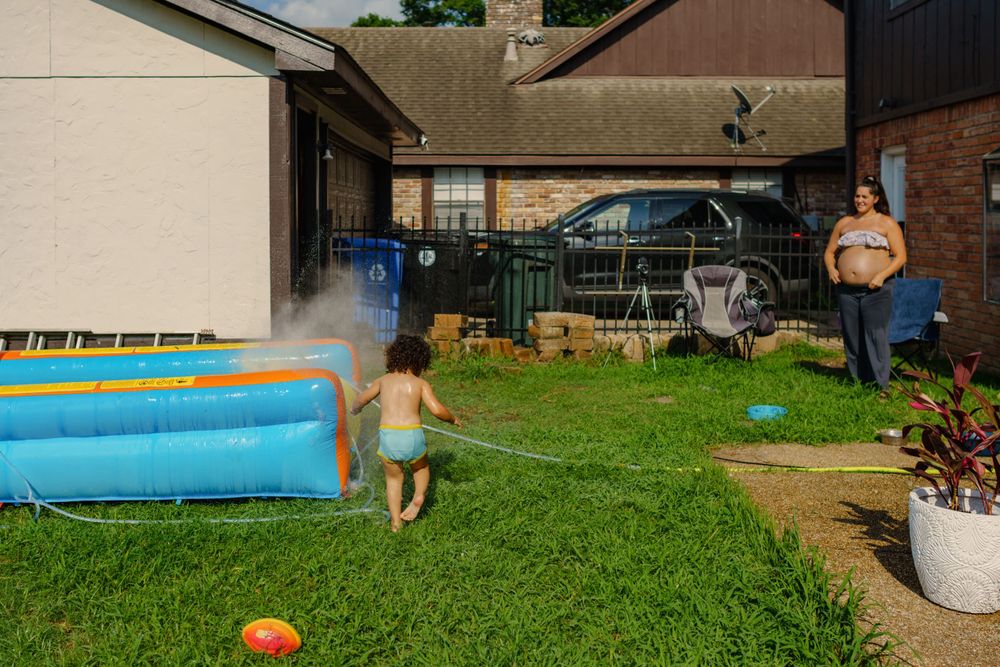 People enjoy a fun summer day playing with an inflatable water slide and pool in a backyard.