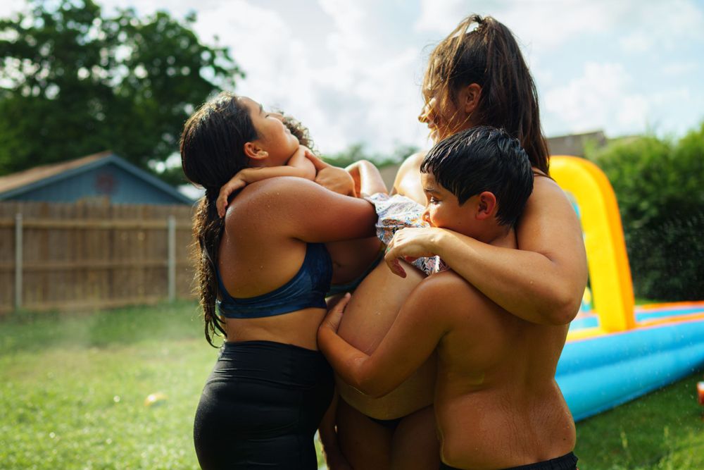 Intimate family moment captured outdoors with a fence and inflatable pool in the background.