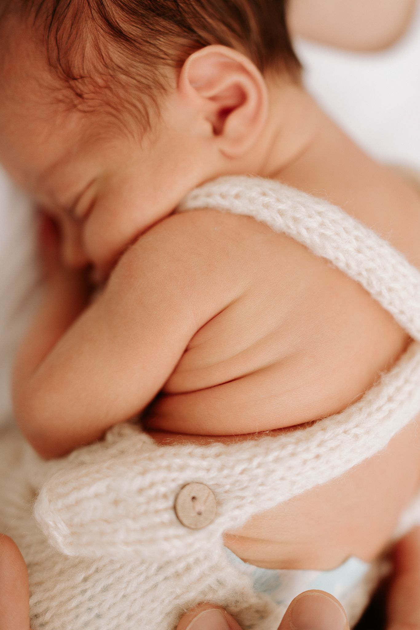Sleeping newborn baby in a cream knit romper with button detail, curled up peacefully.