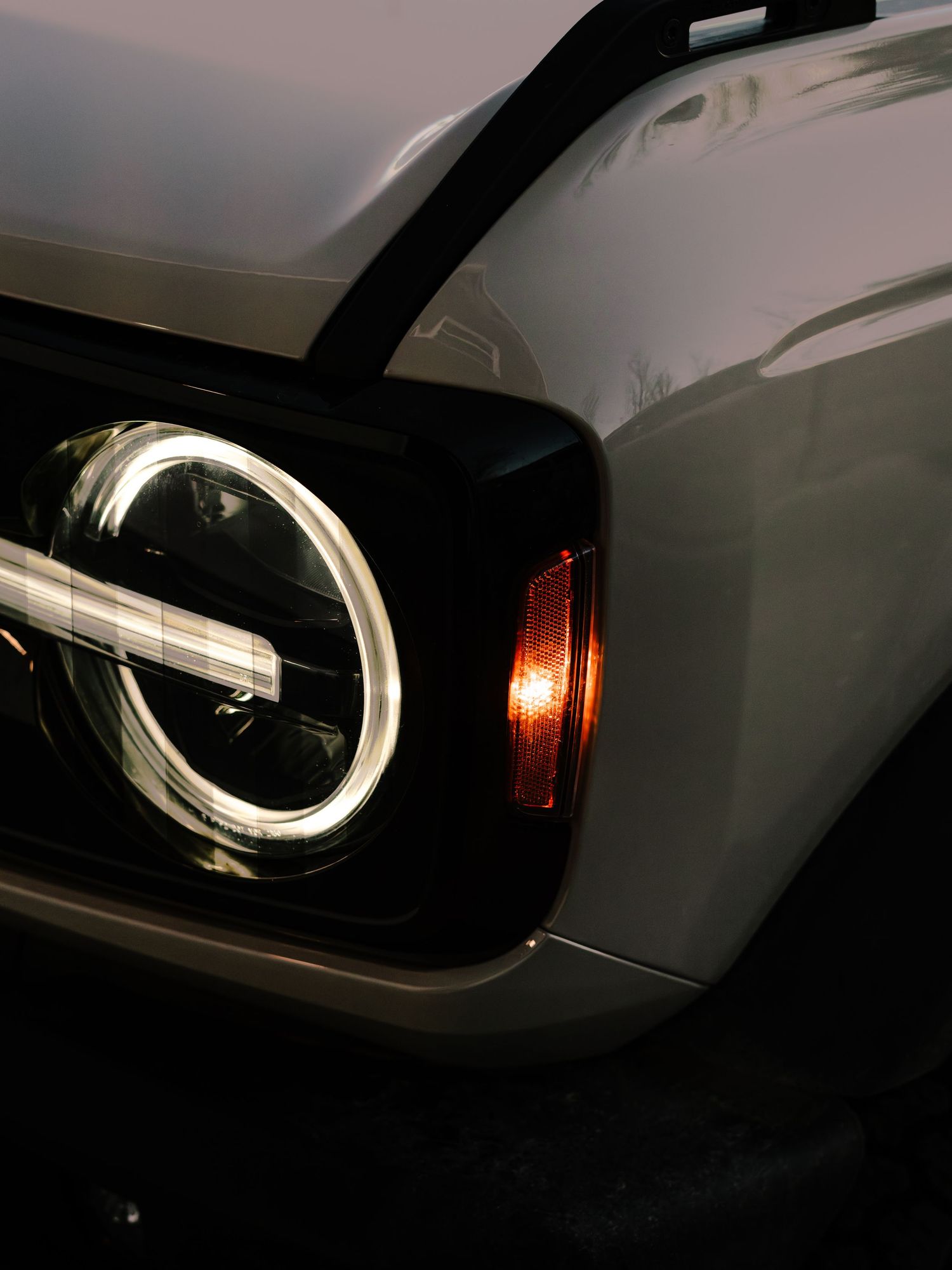 Close-up of a modern car headlight featuring a circular LED daytime running light and amber turn signal in dark setting.