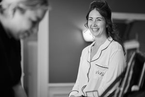 Black and white photo of a smiling woman in white pajamas laughing joyfully indoors.