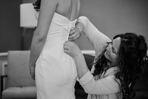Mother helps bride button up her elegant white wedding dress in a black and white photo.