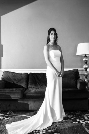 Bride in elegant strapless white gown with train poses in black and white portrait beside a leather sofa.