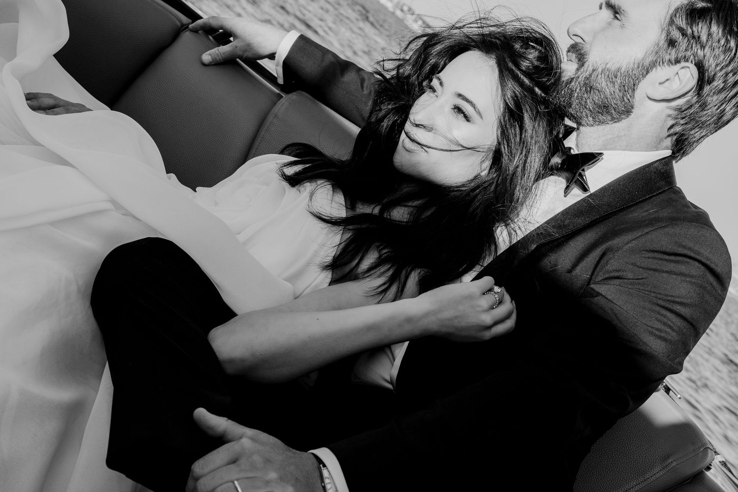Black and white photo of a couple embracing romantically, woman with flowing dark hair clutching mans suit jacket.