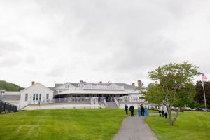 A large white building on a green lawn under cloudy skies with people walking along a path.