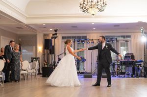 Bride and groom share their first dance in an elegant ballroom with chandeliers and a live band at their wedding reception.