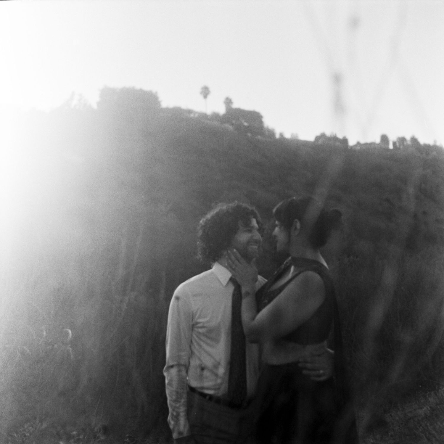 Black and white photo of couple sharing intimate moment against rocky hillside in bright sunlight.
