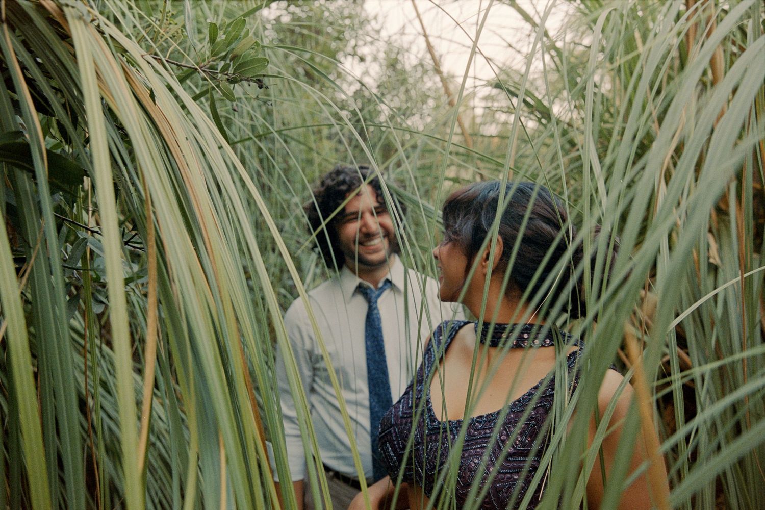 Smiling couple gazing at each other surrounded by lush green tropical foliage outdoors.