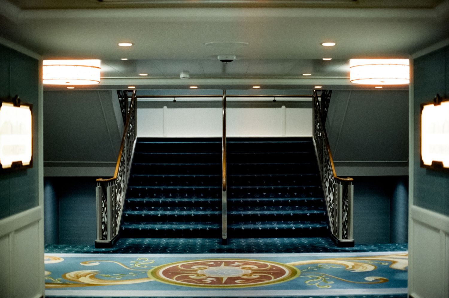 Elegant grand staircase with ornate railings, blue carpet, and decorative floral medallion in a luxurious interior foyer.