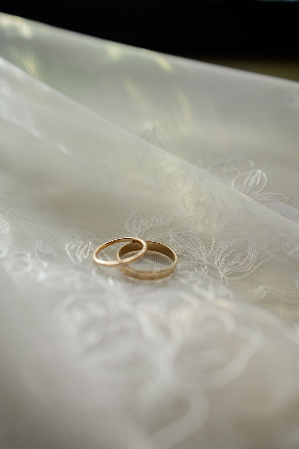 Two gold wedding bands resting on white embroidered bridal fabric, symbolizing love and commitment.