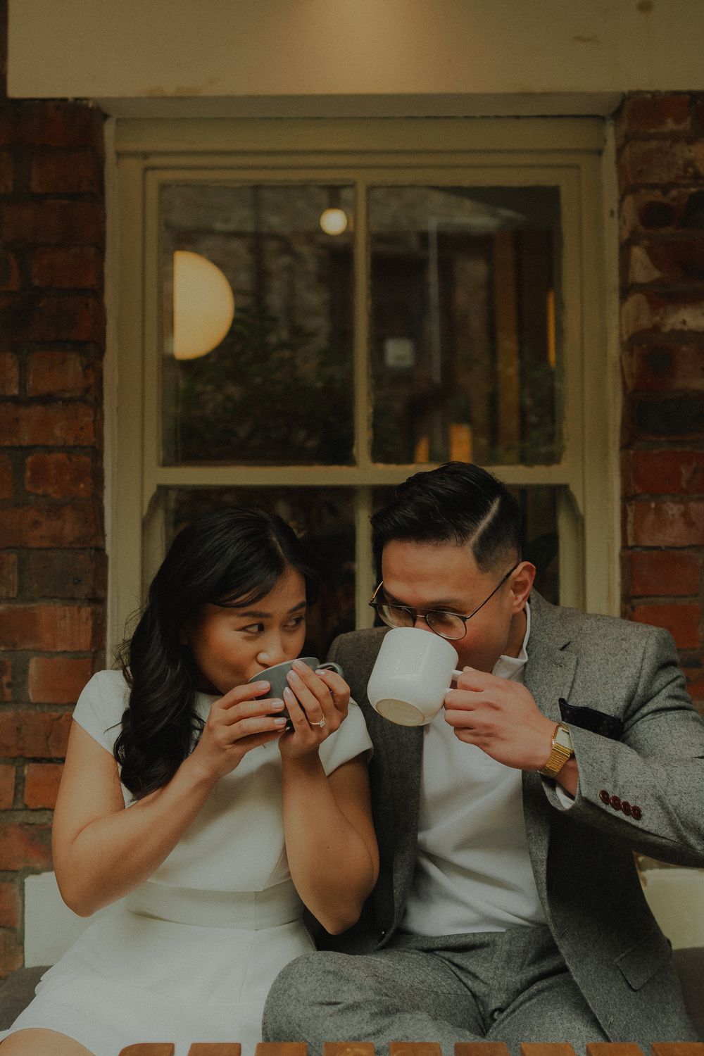 Couple sharing an intimate moment drinking from white mugs outside a brick building.