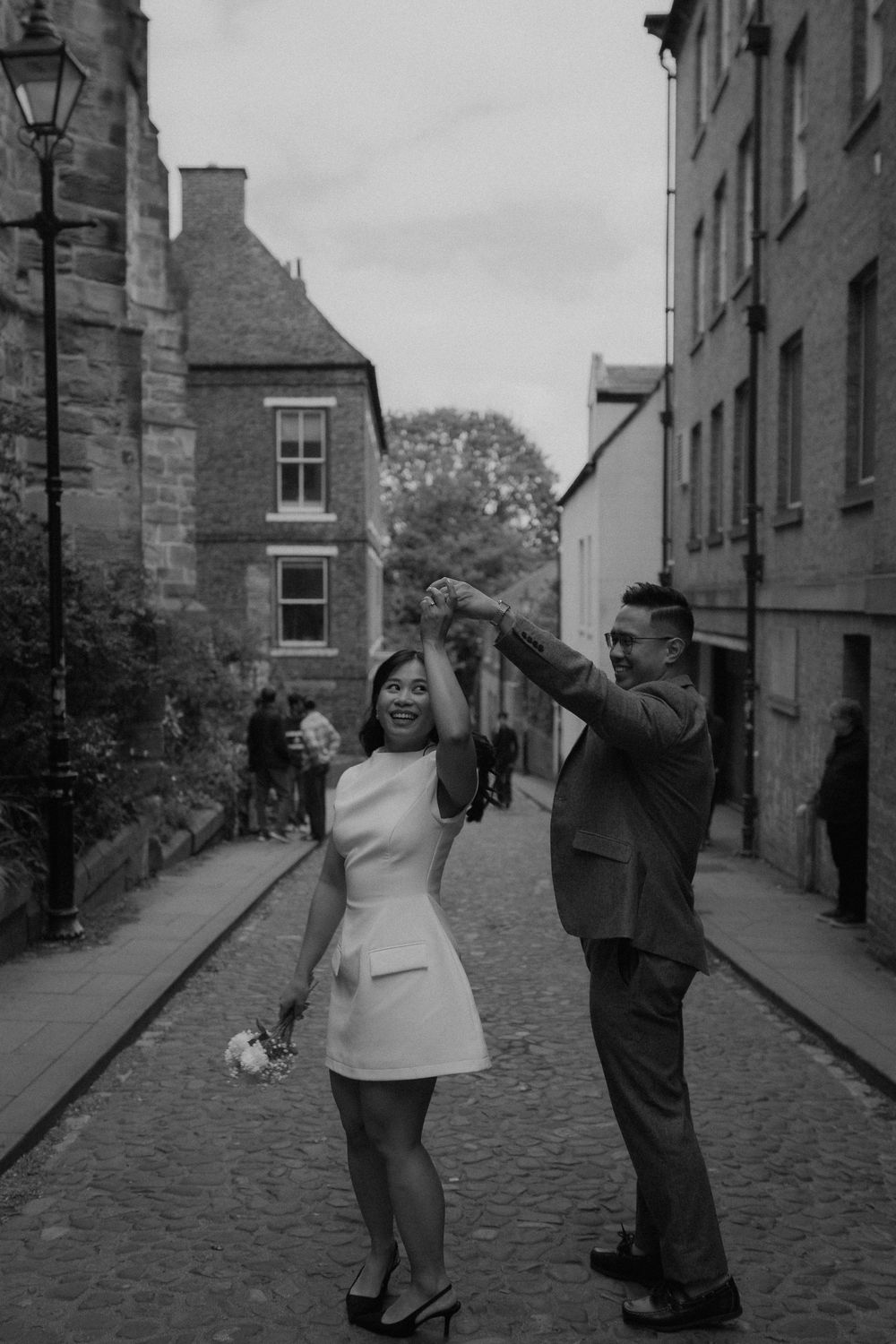 Black and white photo of a couple dancing on a cobblestone street in Edinburgh, woman in mini dress, man in suit.