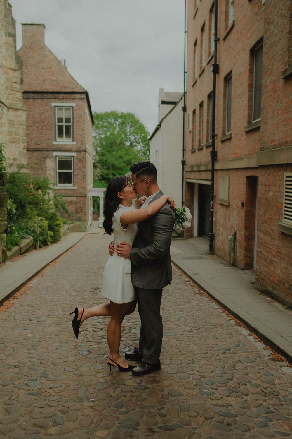 Couple sharing a romantic kiss on a cobblestone alley between historic brick buildings on their wedding day.