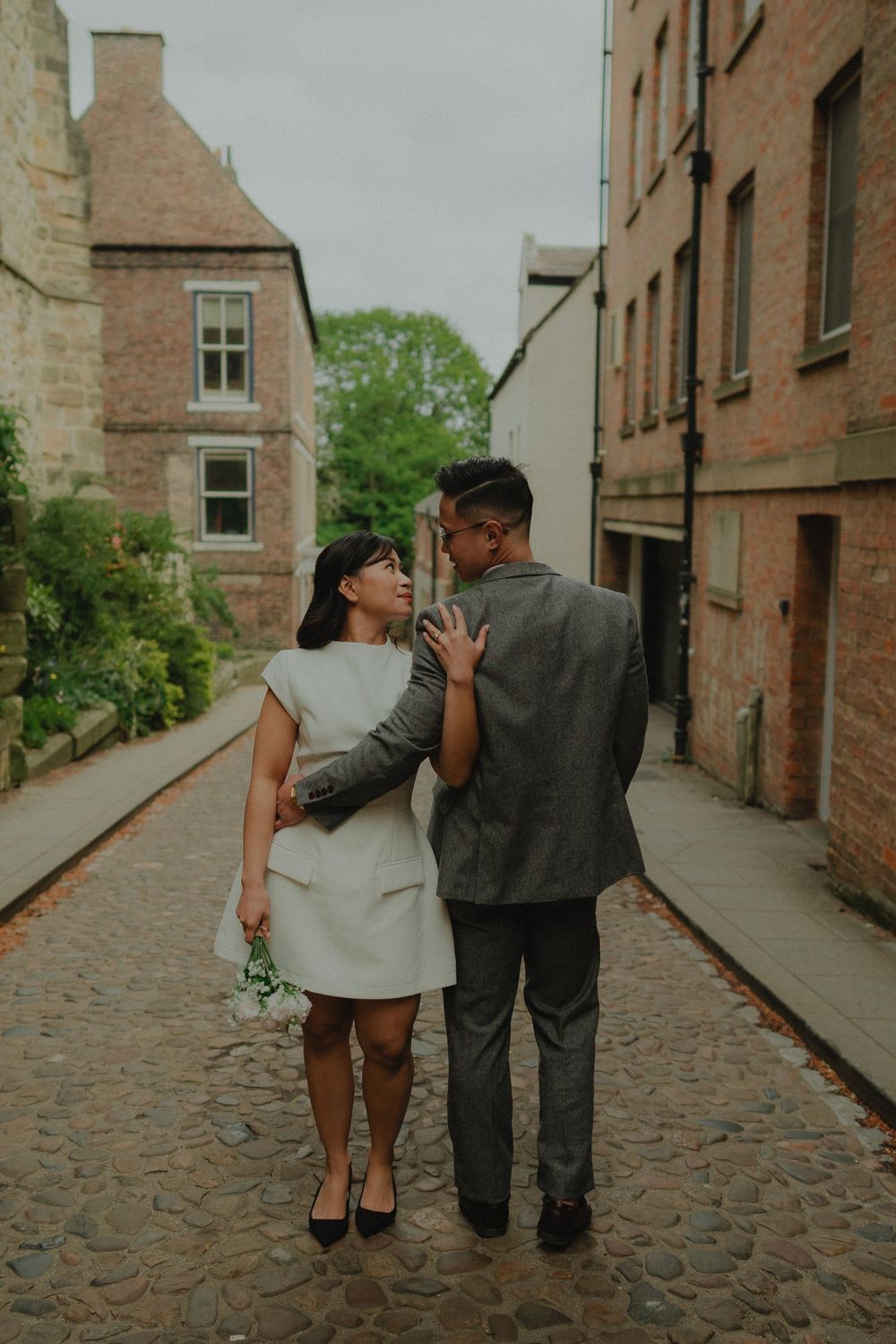 Couple in wedding attire embracing on a cobblestone street in Edinburgh, surrounded by historic stone buildings.