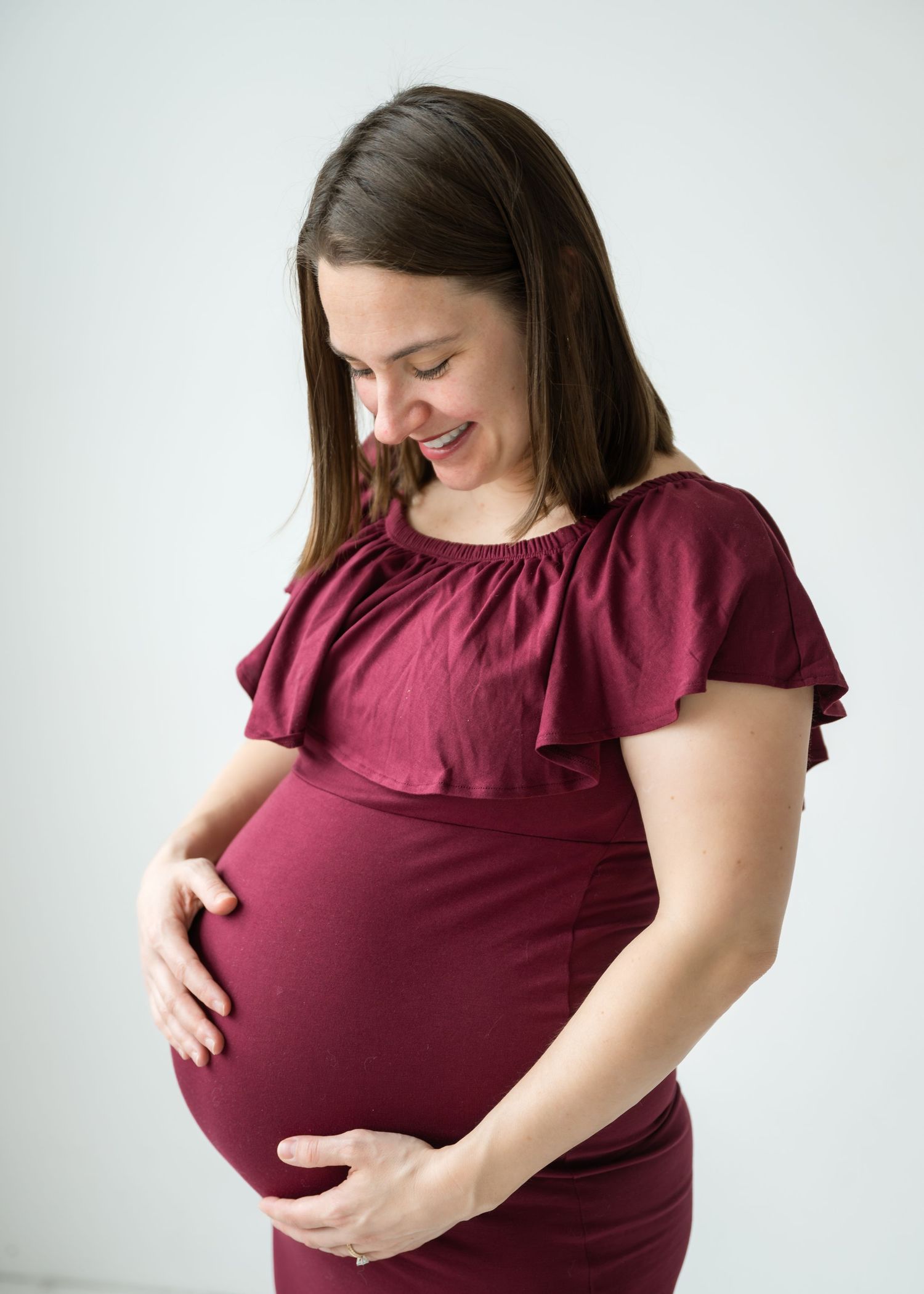 Smiling pregnant woman in burgundy dress cradling her baby bump during a maternity photo session.