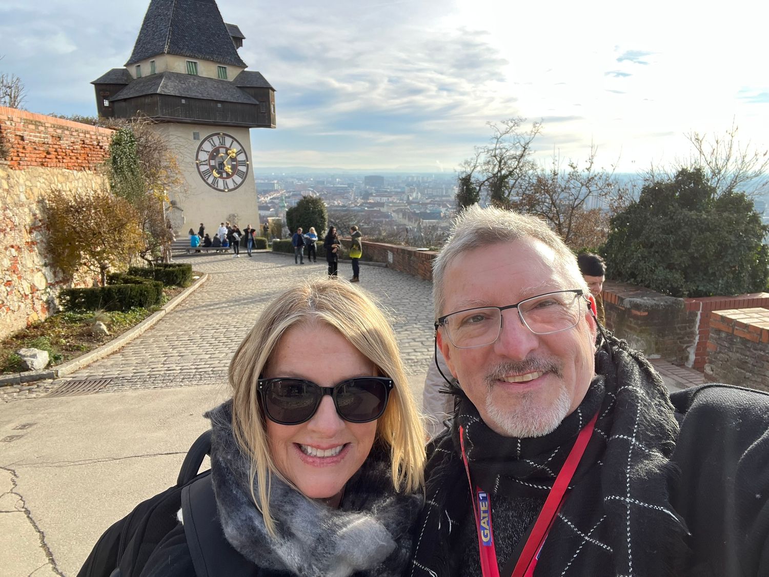 Couple taking a selfie in front of the Graz Clock Tower with panoramic city views on a sunny winter day.