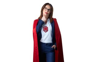 Woman in red superhero cape and glasses poses confidently in business casual attire with shield emblem logo.