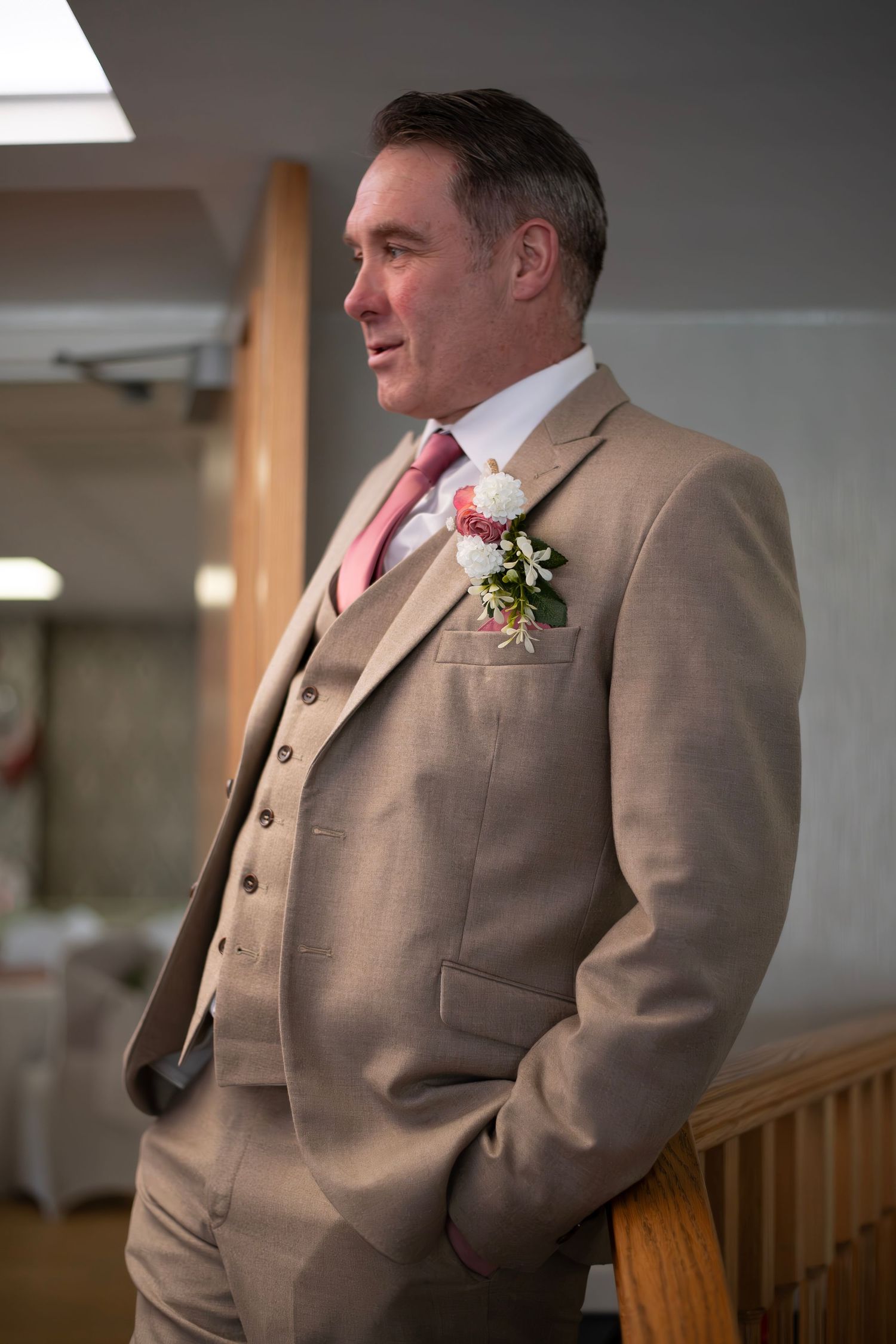 Dapper groom in a tan three-piece suit with pink tie and floral boutonniere at his wedding.